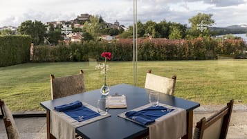 Mesa de comedor al aire libre con vistas a un jardín exuberante y edificios lejanos.