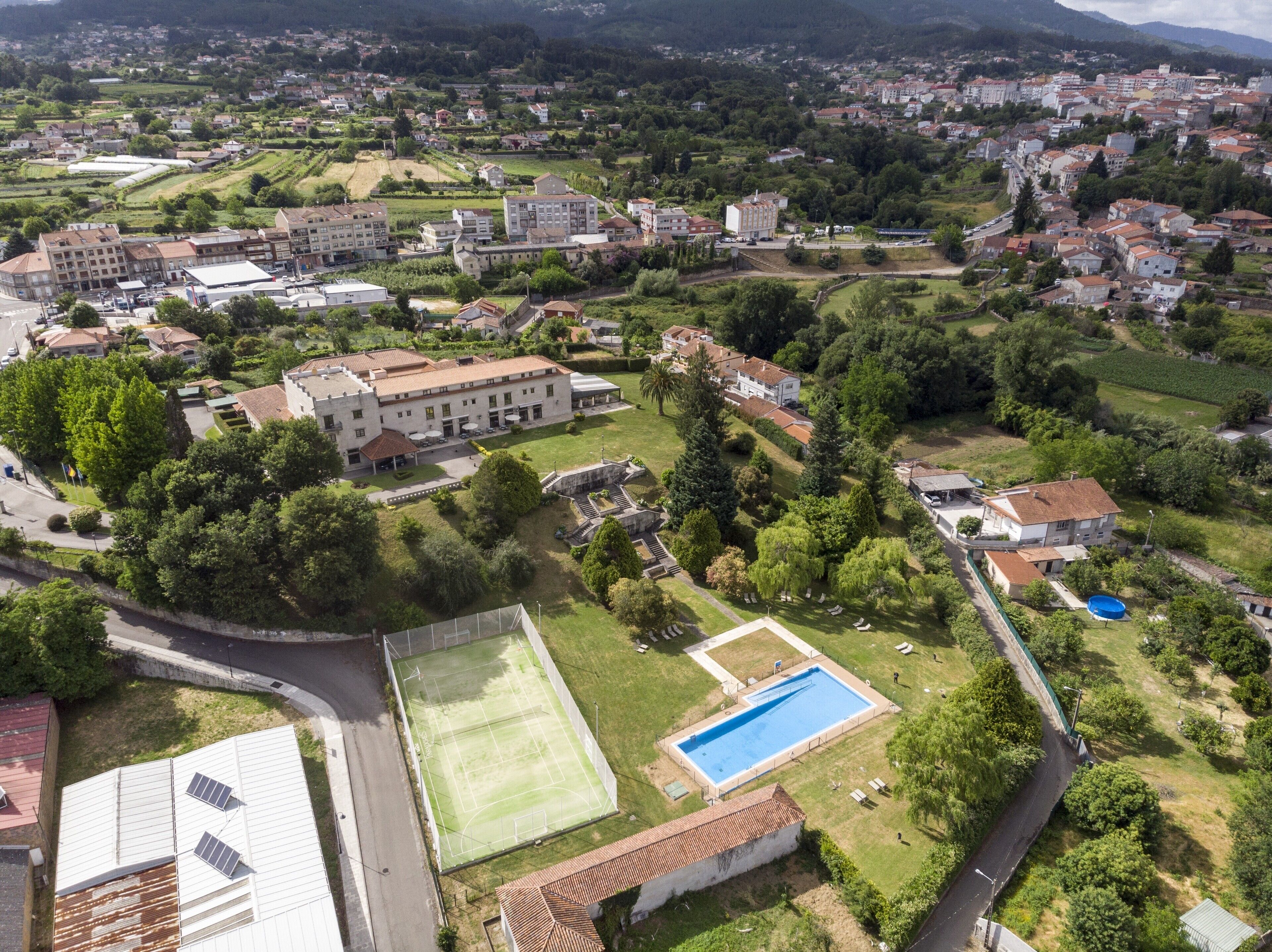 An aerial view of a residential area with a large building, a swimming pool, and surrounding greenery.