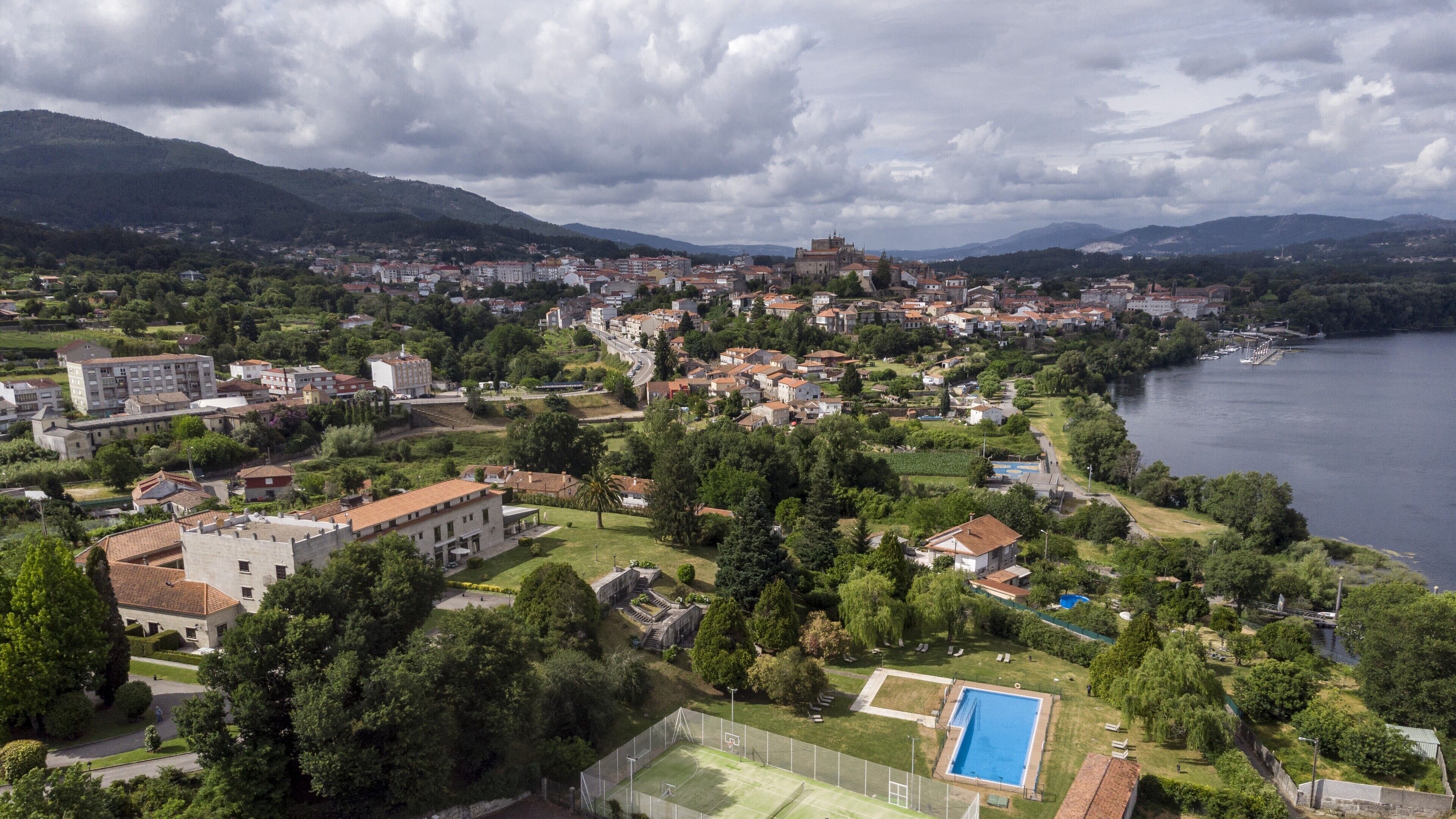 An aerial view of a coastal town with a prominent castle-like building, a large swimming pool, and a river.