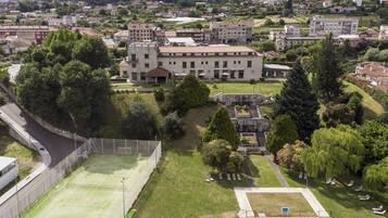 A large building with a swimming pool, tennis court, and surrounding greenery.