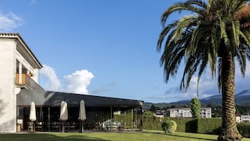 A modern building with a covered outdoor seating area, palm trees, and a view of the surrounding landscape.