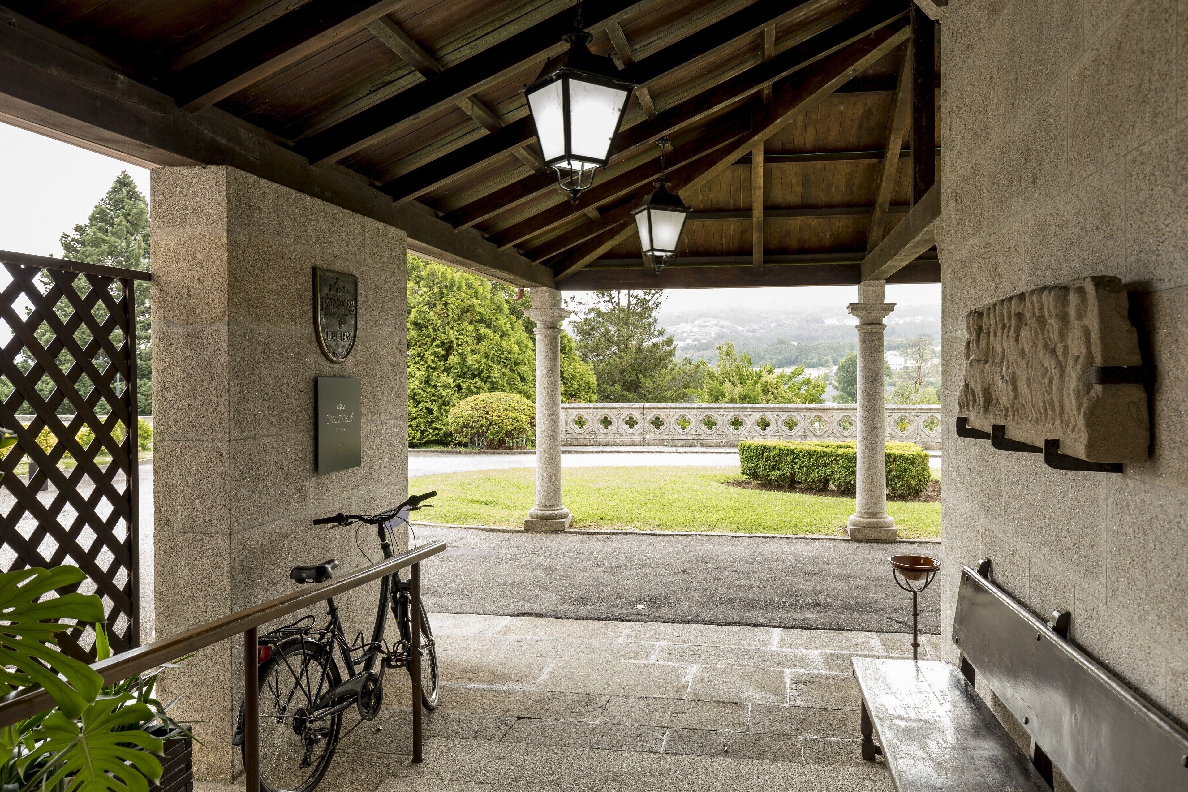 Un espace extérieur abrité comprenant un vélo, un banc et une vue sur un jardin et une route.