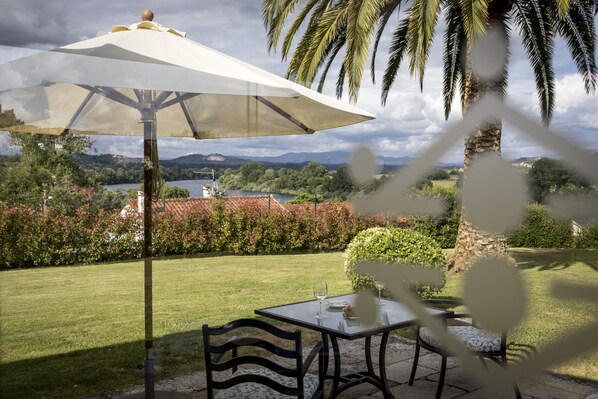 Un patio con una mesa, sillas, una sombrilla y vistas a un lago y montañas.