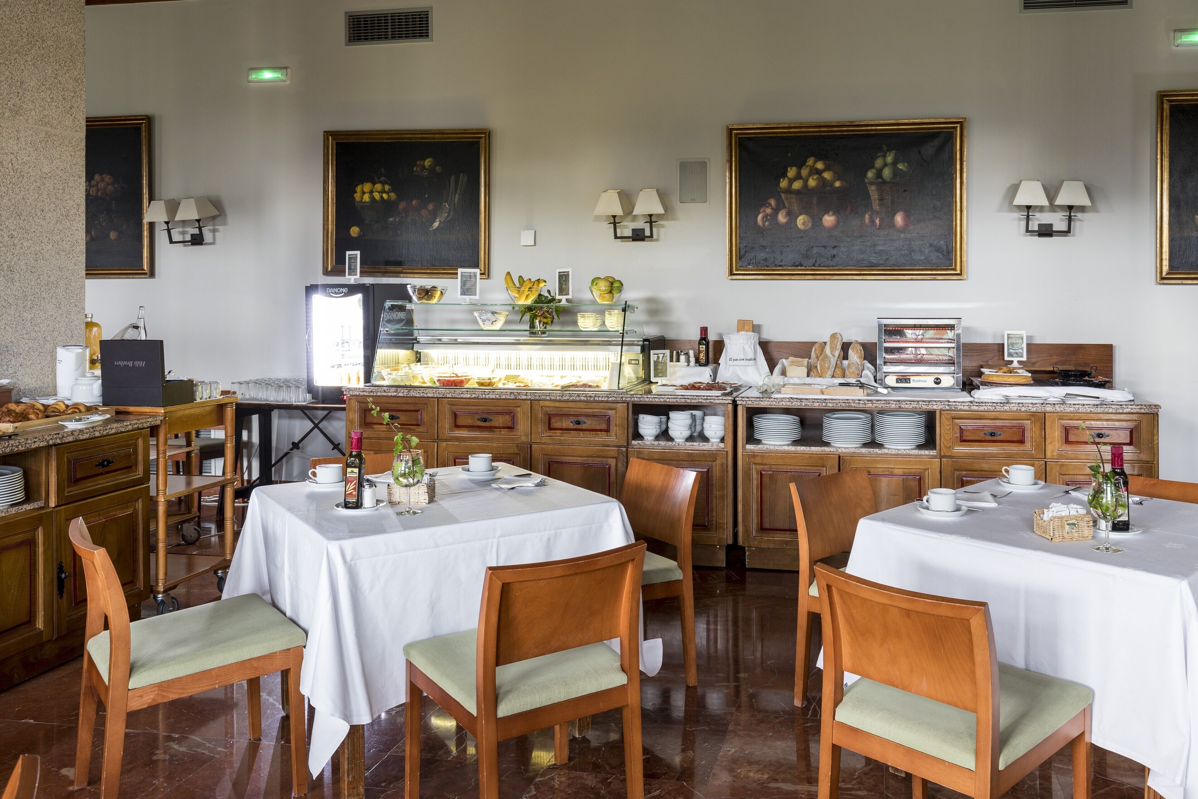 Un restaurant avec des chaises et des tables en bois, un espace buffet et des œuvres d’art accrochées aux murs.