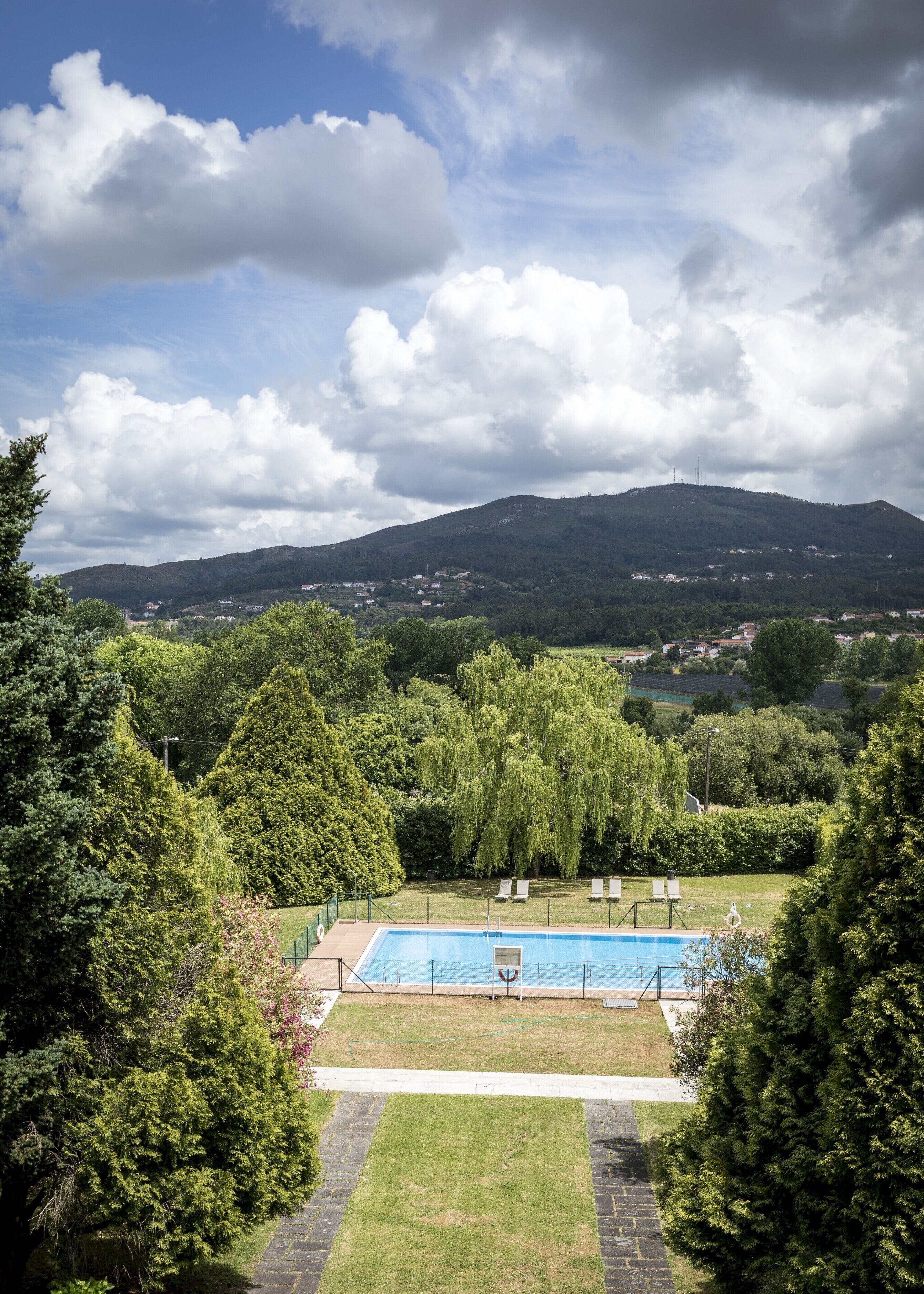 Una piscina rodeada de árboles, con vista a una colina y edificios a la distancia.