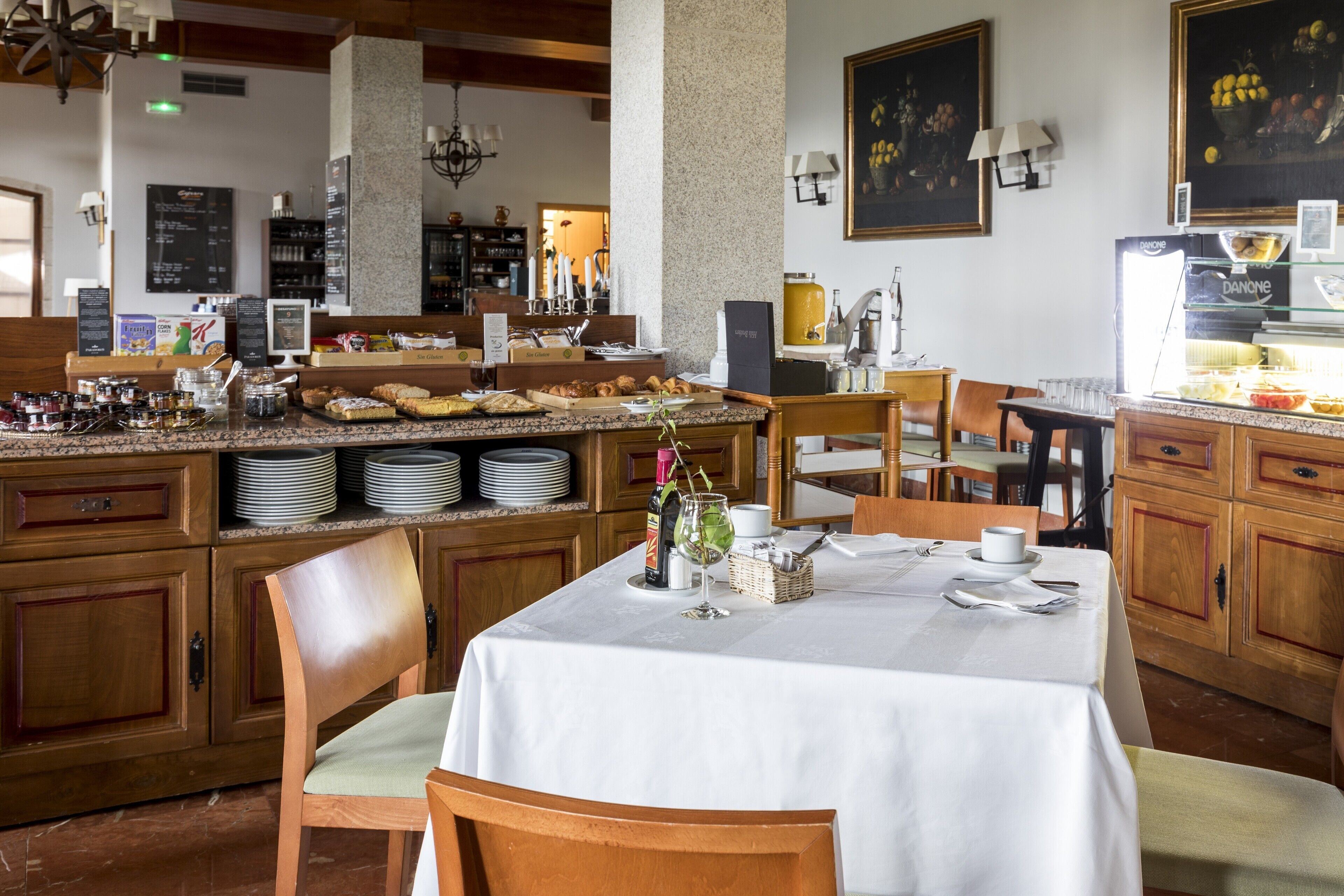 A breakfast area with a buffet, wooden cabinets, and a white tablecloth-covered table.