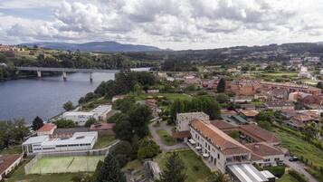 Un quartier résidentiel traversé par une rivière, avec un pont et un grand bâtiment abritant un terrain de sport.