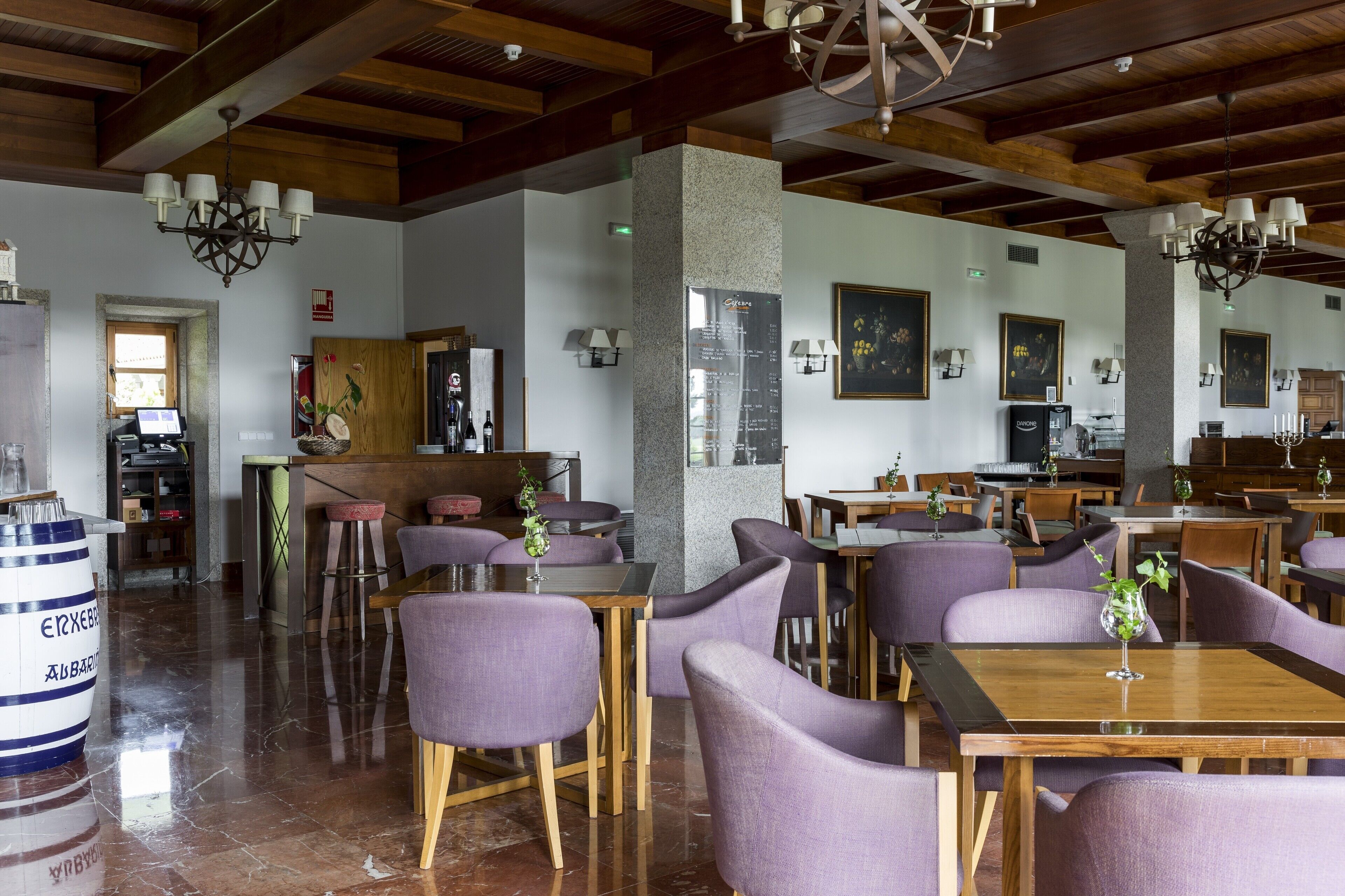 A spacious restaurant with wooden tables and purple chairs, a stone pillar, and a chandelier.
