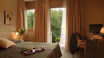 A hotel room with a bed, a desk with a TV, and a window with curtains.