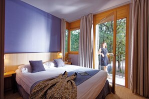 Relax in this inviting room with a large bed, wooden headboard, and a window offering a view of lush greenery.