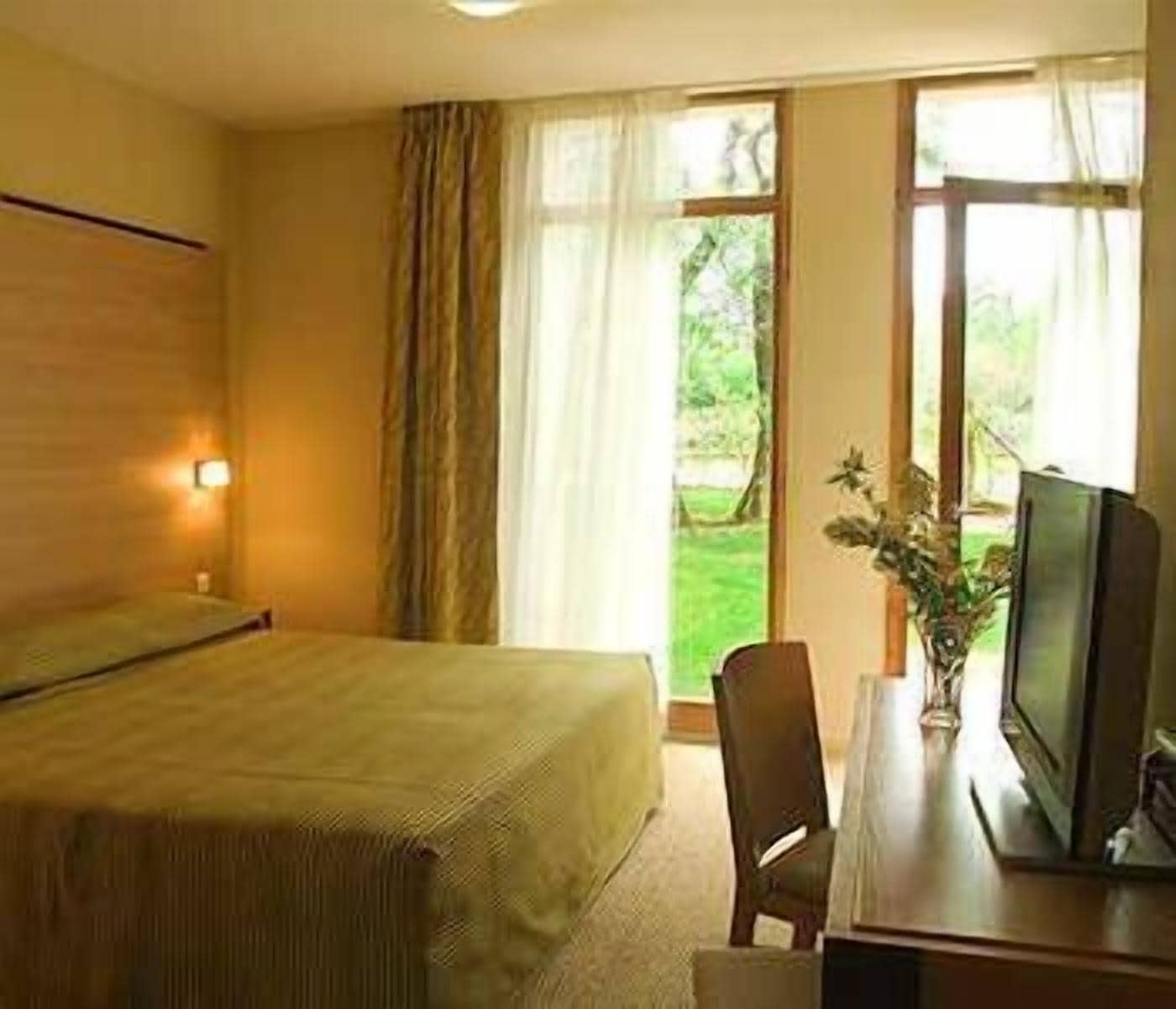 A hotel room with a bed, a desk with a television, and a window with curtains.