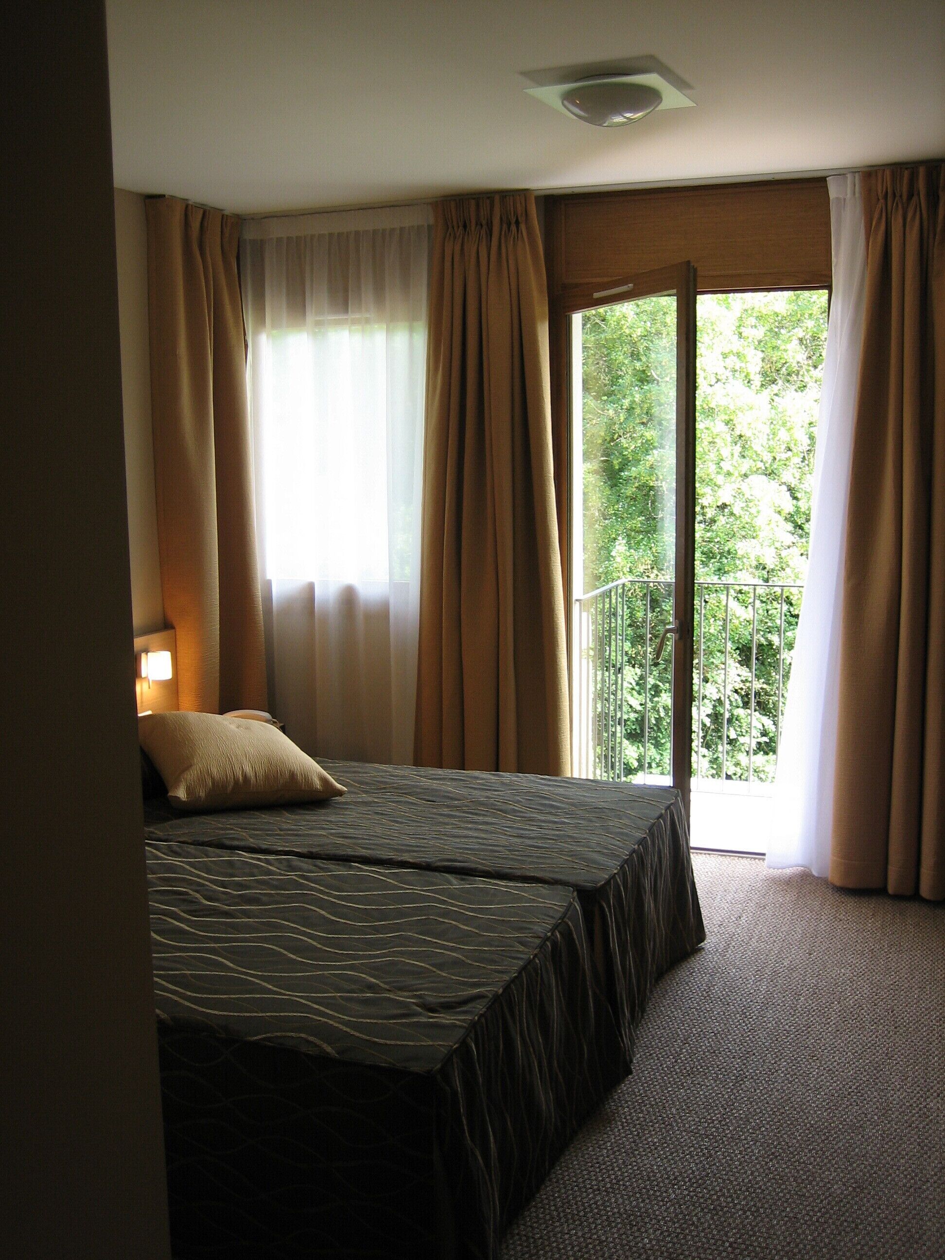 Una habitación de hotel con cama, ventana con cortinas y vista a la vegetación.