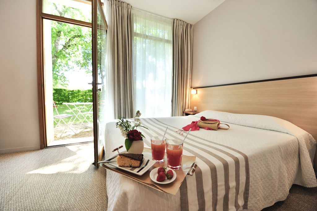 A hotel room with a bed, a tray with food and drinks, and a view of greenery outside.