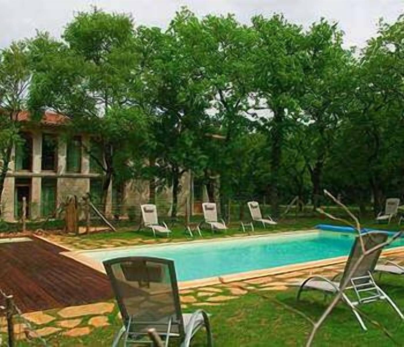 Une piscine entourée de chaises longues, de verdure luxuriante et d’un bâtiment en pierre.