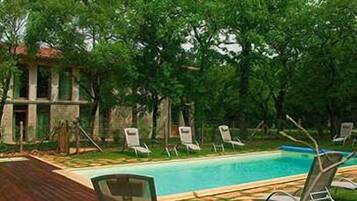 A swimming pool with lounge chairs, surrounded by lush greenery and a stone building.
