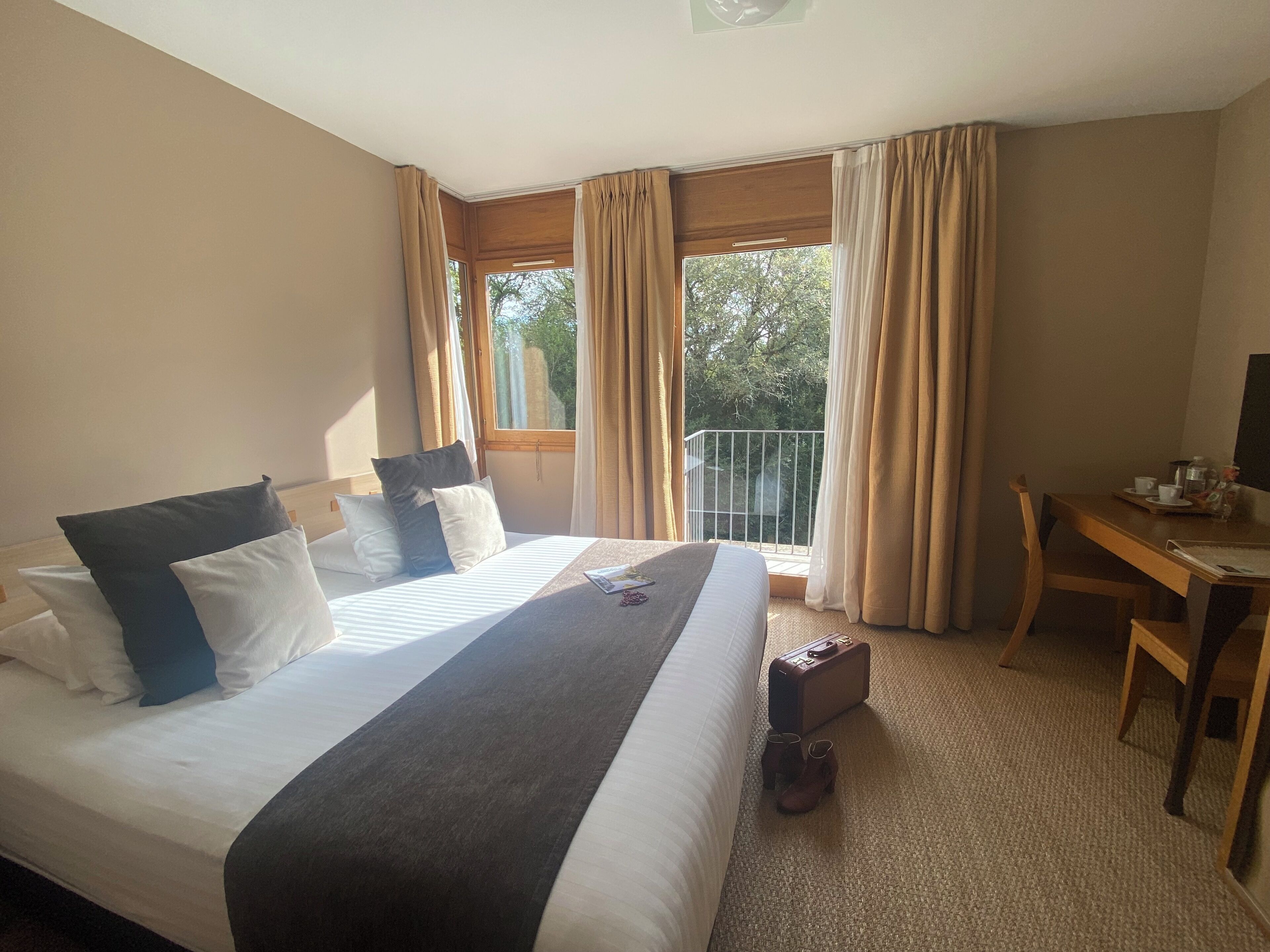 A hotel room with a large bed, a desk, and a balcony with curtains.