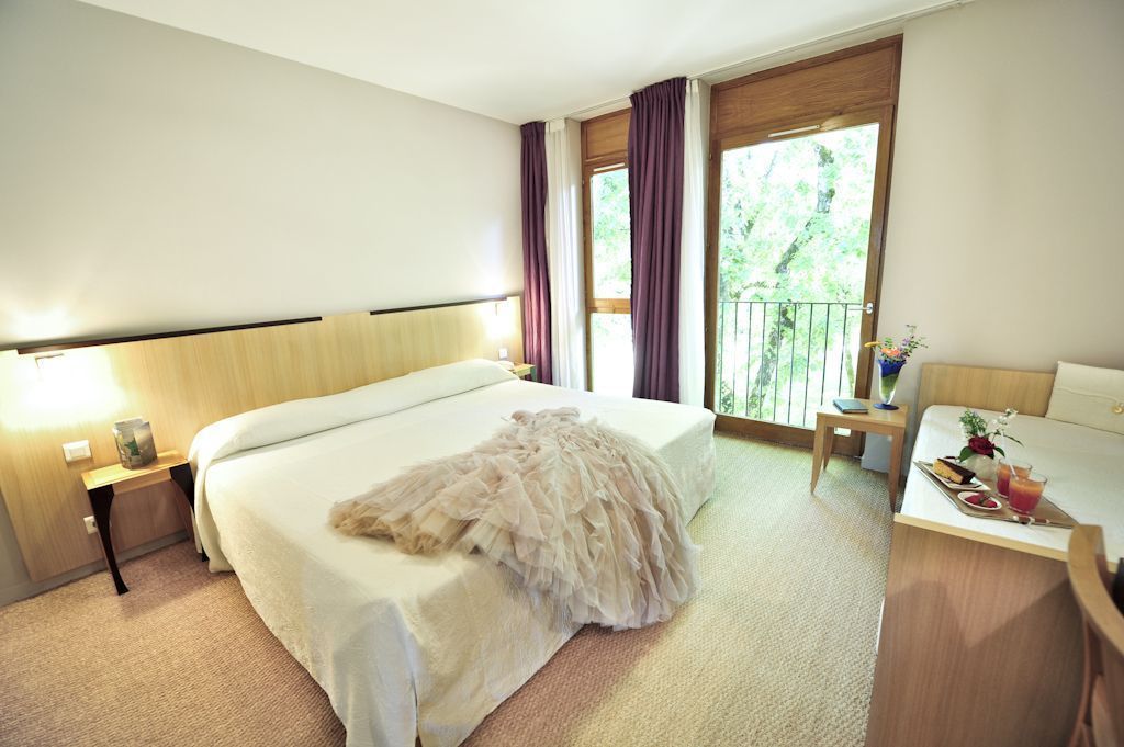 A hotel room with a large bed, a desk, a chair, a nightstand, and a window with curtains.