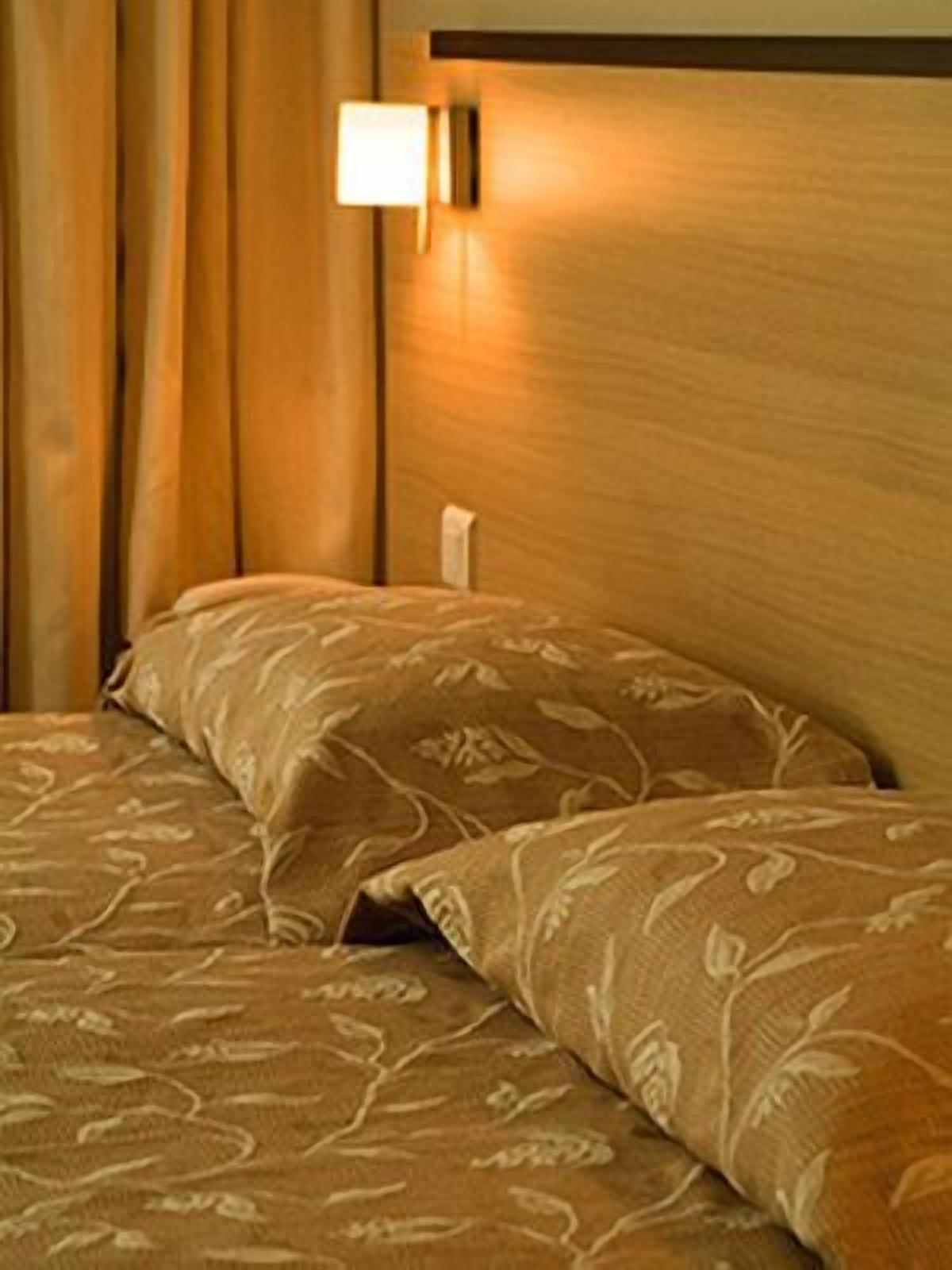 A hotel room with a wooden headboard, a bedside lamp, and a bed with patterned bedding.