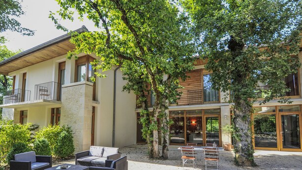 A modern two-story building with a balcony, outdoor seating area, and a gravel patio.
