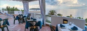 Un área de comedor al aire libre con mesas y sillas, con vistas a una masa de agua y una isla distante.