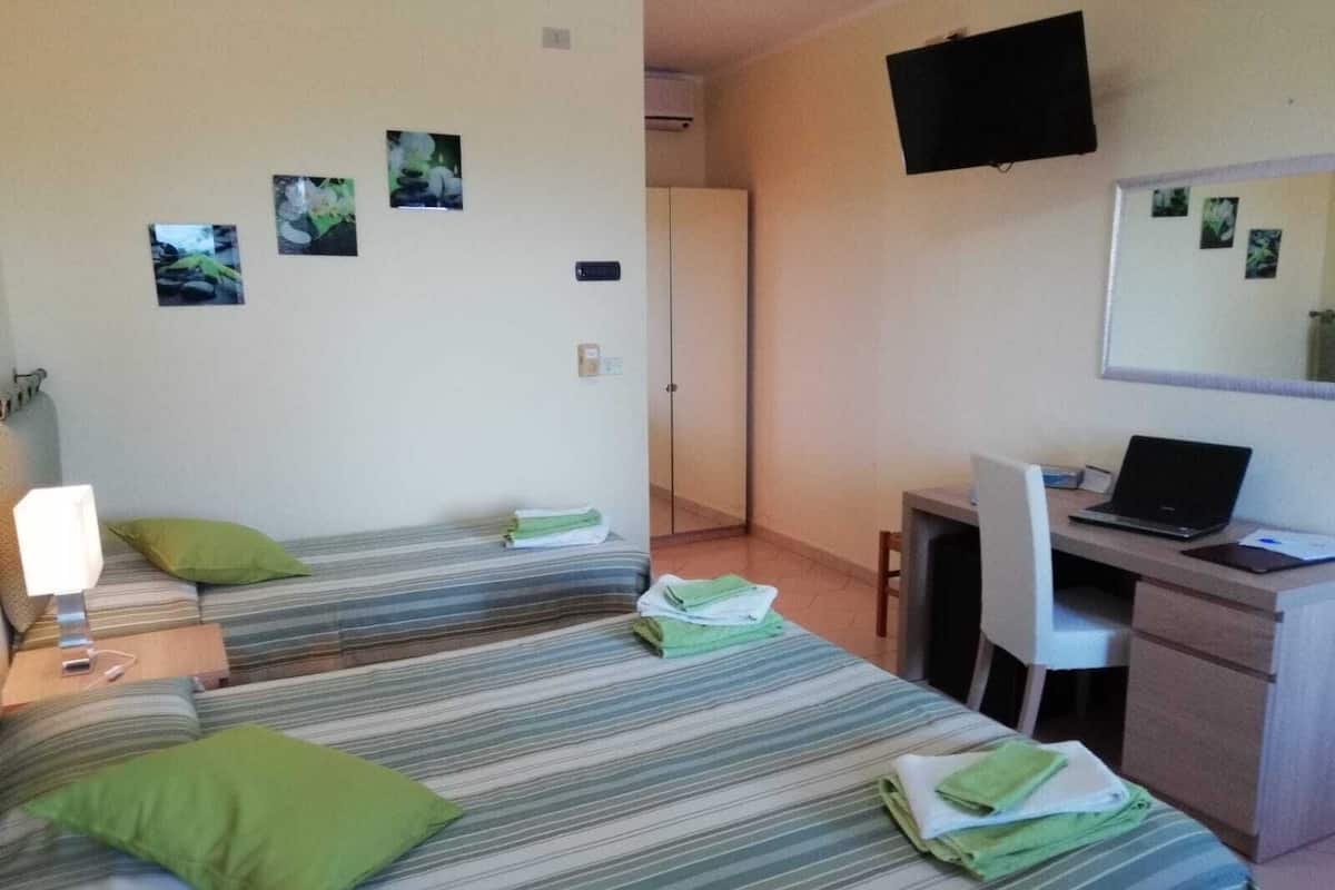 A room with two beds, a desk with a laptop, a chair, and a TV mounted on the wall.
