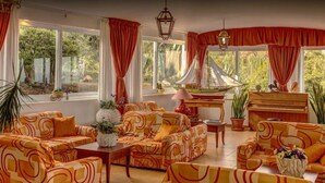 A spacious living room with large windows, a piano, and patterned sofas. - Calabattaglia (Ventotene)