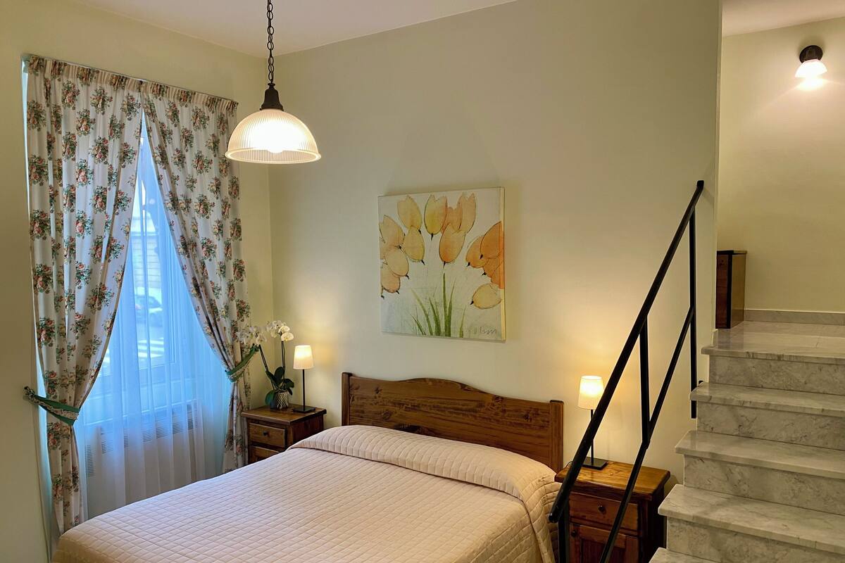 Une chambre à coucher avec un lit, une table de chevet, une lampe, un tableau et un escalier.