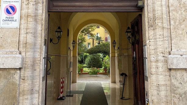 Ein gebogener Eingang mit einer Steinfassade, ein Verbotsschild und der Blick auf einen Innenhof mit einem Weg, der zu einem Gebäude führt.