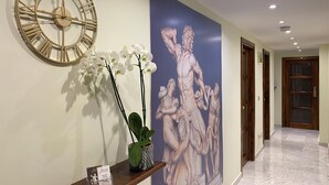 Ein Flur mit einer großen Wanduhr, einem Blumentopf, einem gerahmten Kunstwerk und einem Empfangstresen.
