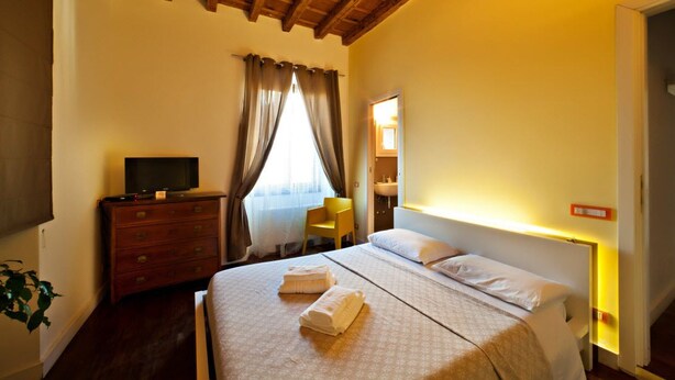 A hotel room with a wooden ceiling, a bed with white linens, a TV on a dresser, and a window with curtains. - B&B SubUrbe Roma (Rome)