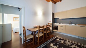 A compact kitchen with wooden cabinets, a dining table with chairs, and a visible stove. - B&B SubUrbe Roma (Rome)