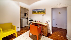 A compact room with a wooden desk, a yellow chair, a small kitchenette, and a painting on the wall. - B&B SubUrbe Roma (Rome)
