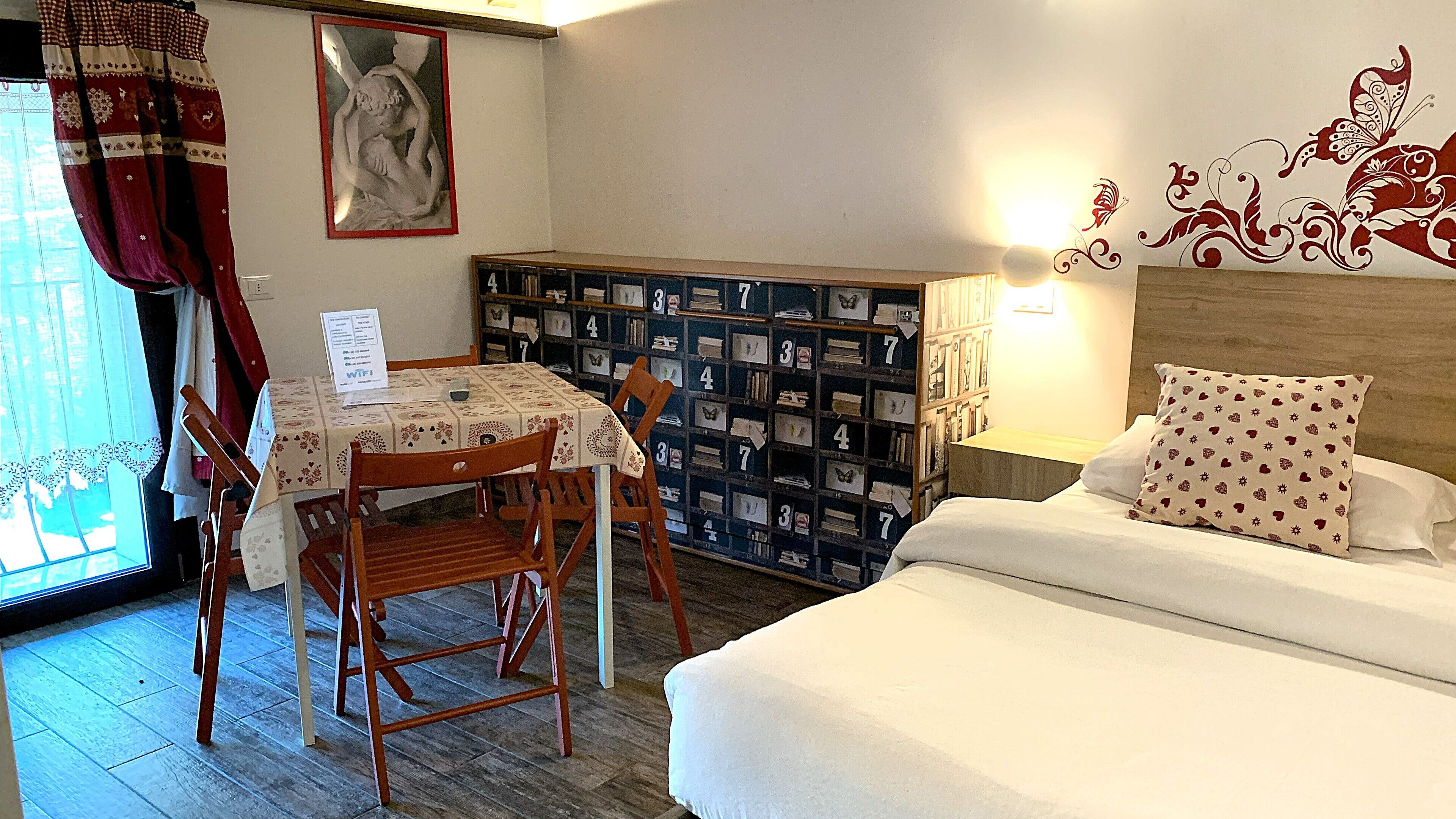 Une pièce comprenant un lit, une table avec des chaises, une bibliothèque et une fenêtre avec des rideaux.