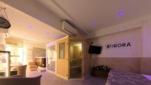 Zona de recepción de hotel con un mostrador de madera, una puerta de vidrio que da a una sauna y un televisor montado en la pared.