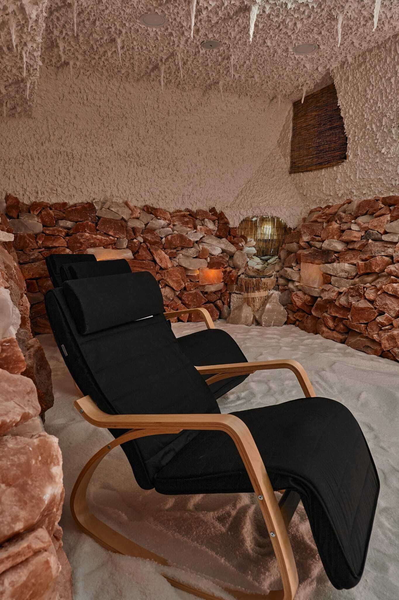 A spa room with a stone wall, a wooden chair, and a small table with a candle.