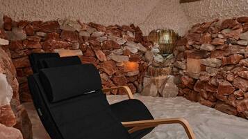 A spa room with a stone wall, a wooden chair, and a small table with a candle.