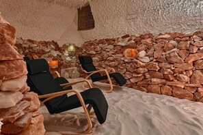 Un cuarto de spa con paredes de piedra, dos sillones negros y una chimenea de piedra.