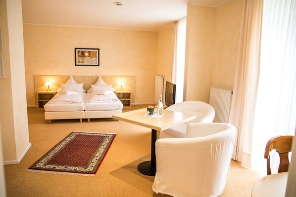 Een hotelkamer met een bed, twee nachtkastjes met lampen, een televisie, een kleine tafel, een stoel en een vloerkleed.