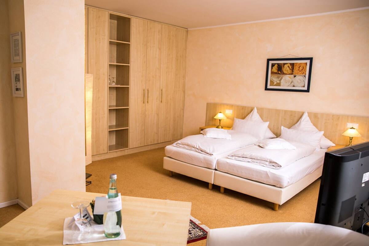 A hotel room with a double bed, bedside lamps, a television, a wooden wardrobe, and a framed picture on the wall.