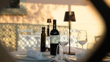 Uma mesa de jantar posta com uma garrafa de vinho, copos e talheres, com uma luminária e uma cadeira ao fundo.