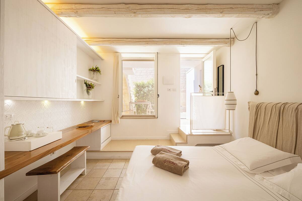 Une chambre moderne avec un banc en bois, un lit avec des serviettes, une table de chevet et une fenêtre.