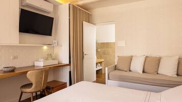 Habitación de hotel con cama, escritorio con silla, televisión, sofá y baño visible a través de una puerta abierta.