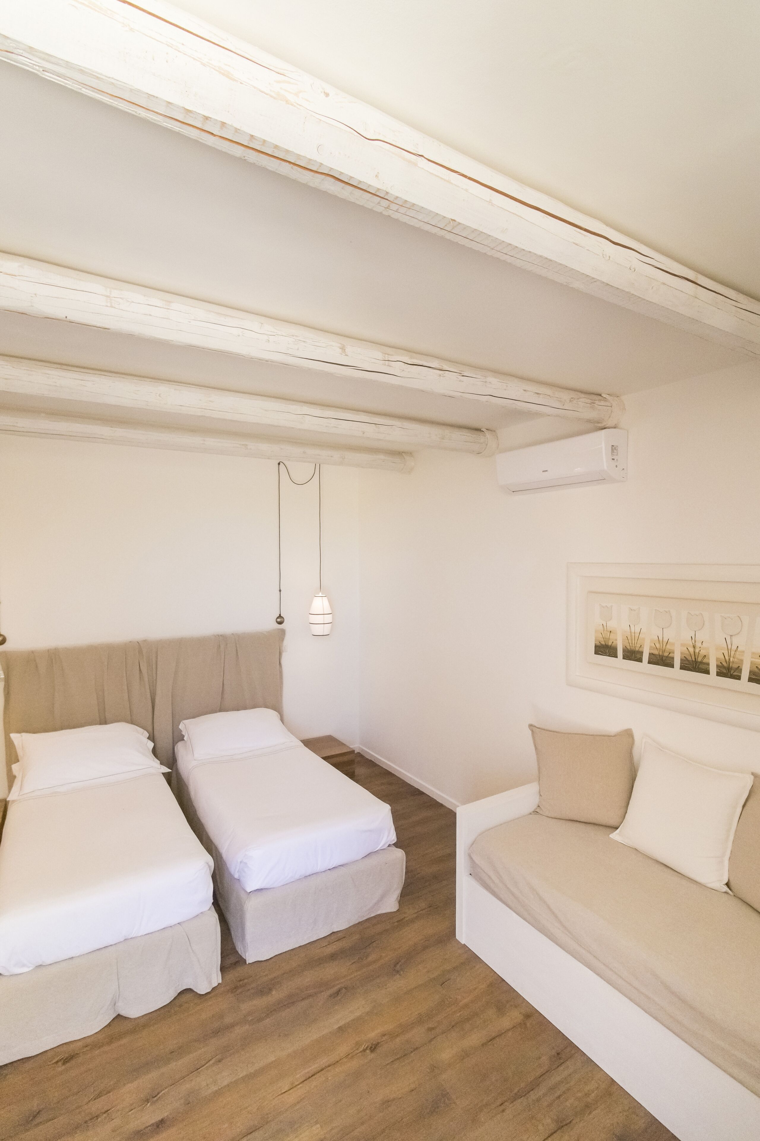 A room with two beds, a sofa, a ceiling fan, and a wall-mounted air conditioner.