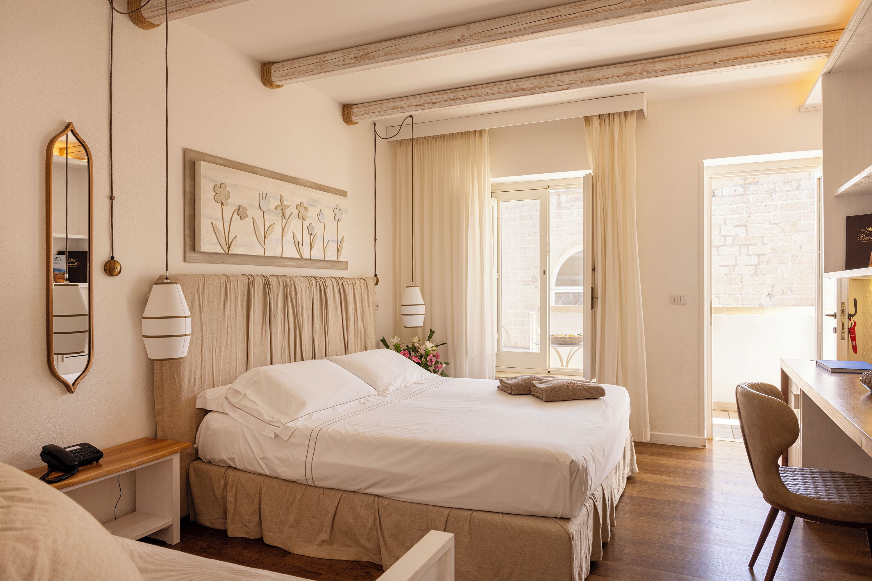 A hotel room with a bed, bedside table, lamp, and a desk with a chair.