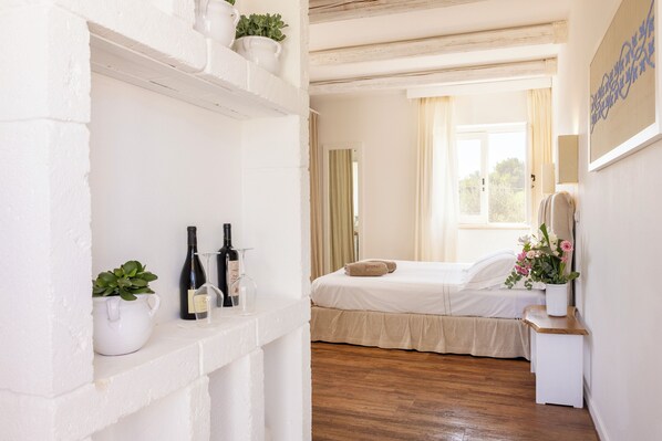 A bedroom with a bed, a bedside table with a vase of flowers, and a shelf with a plant and bottles.
