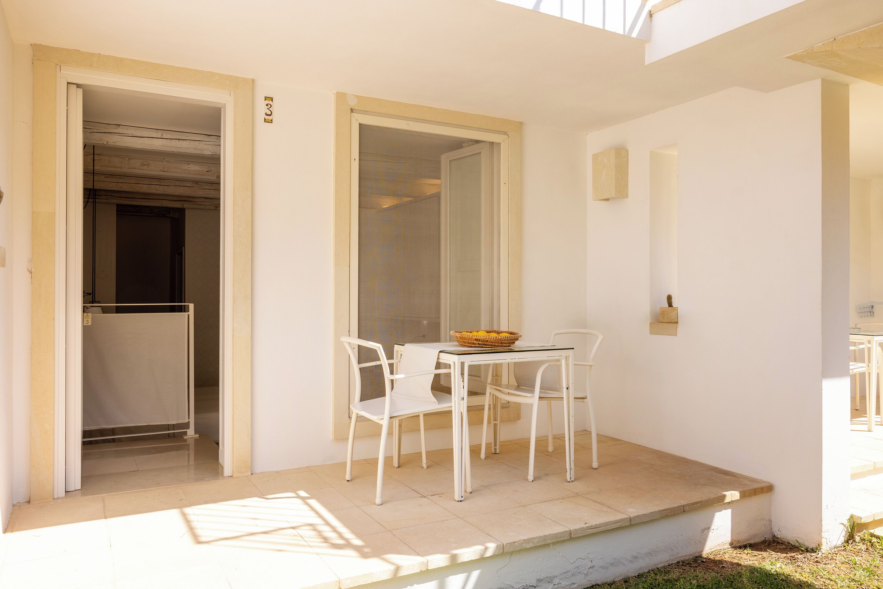 Eine kleine Terrasse im Freien mit Tisch, Stühlen, einem Korb und einer Tür zu einem Innenbereich.