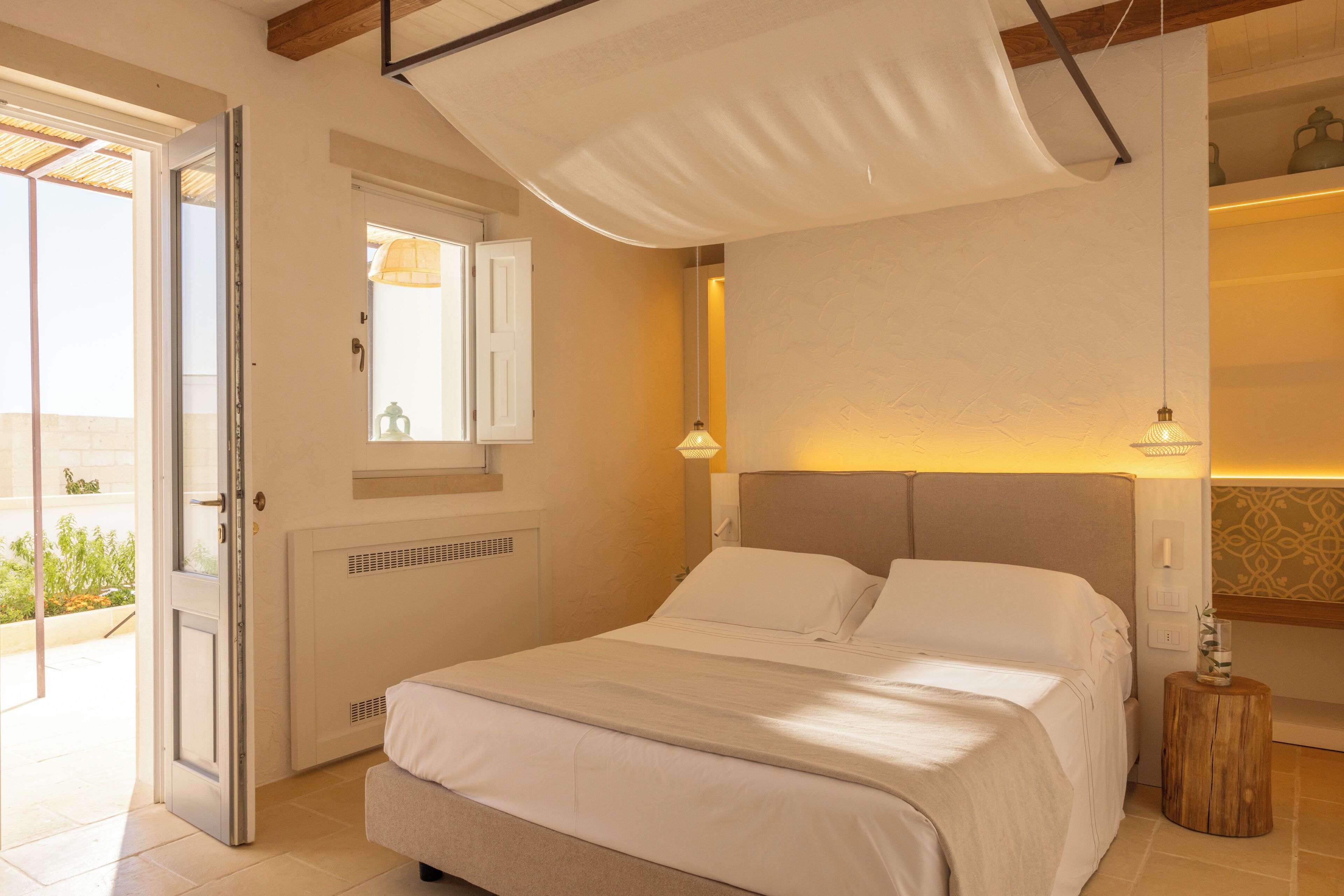 A bedroom with a bed, a window with a view, a bedside table, and a door leading to an outdoor area.