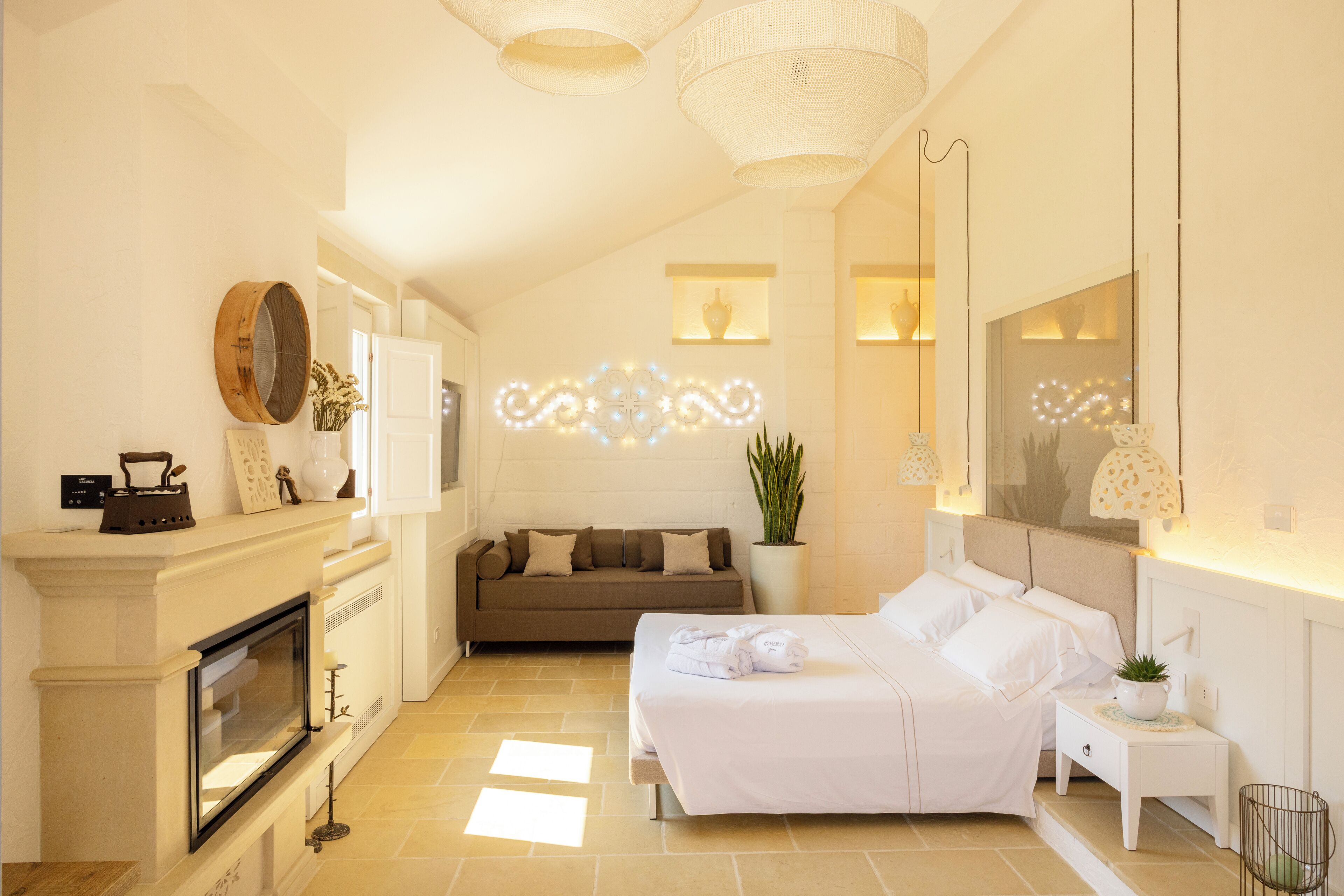 A hotel room with a fireplace, a sofa, a bed, a nightstand, and a mirror.