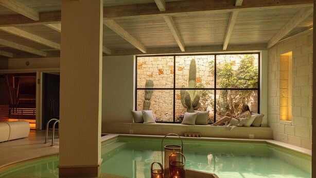 Una piscina interior amb paret de pedra i zona d'seients al costat d'una finestra.