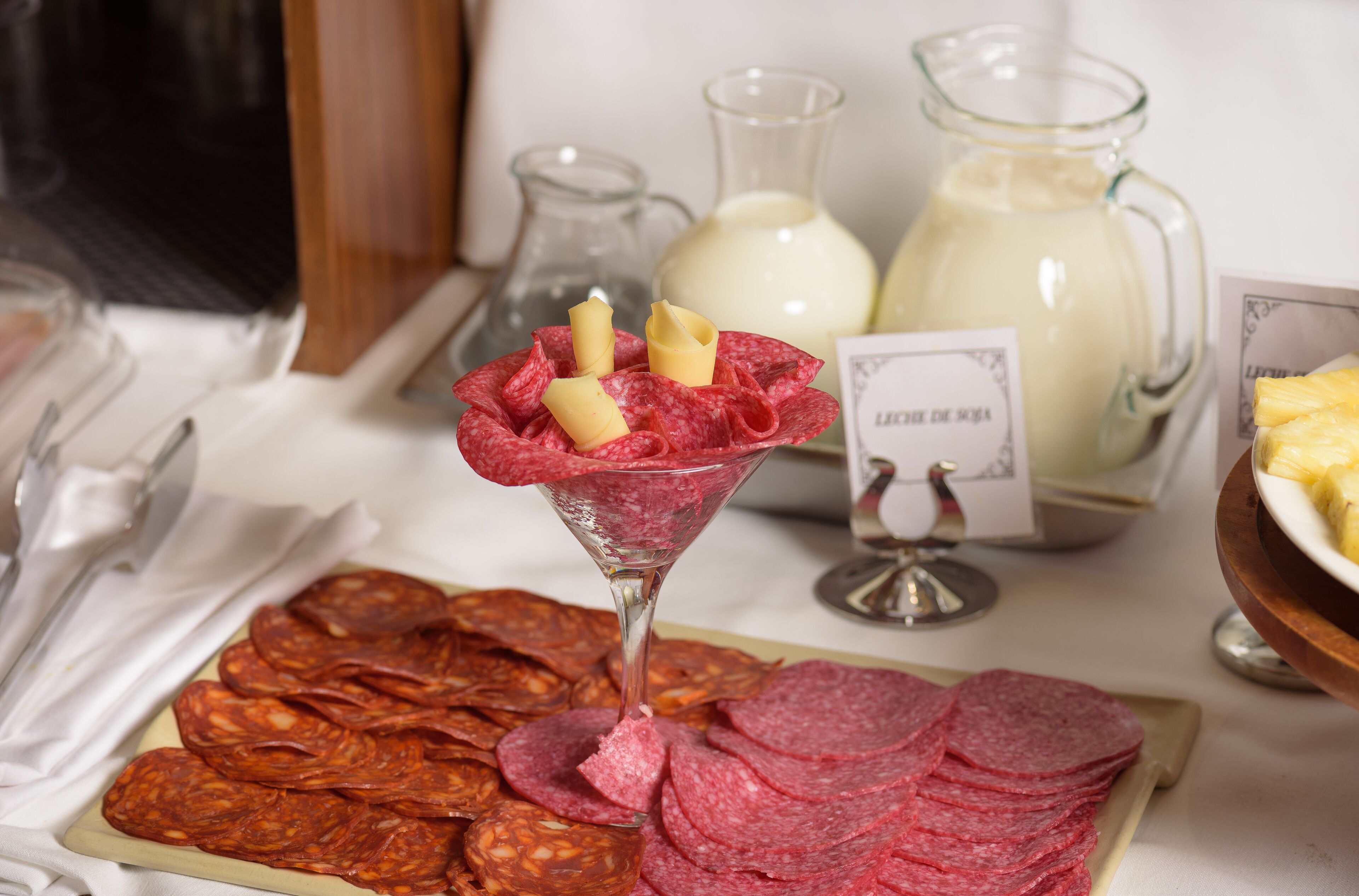 A table with sliced cured meats, a glass of milk, and a candle.
